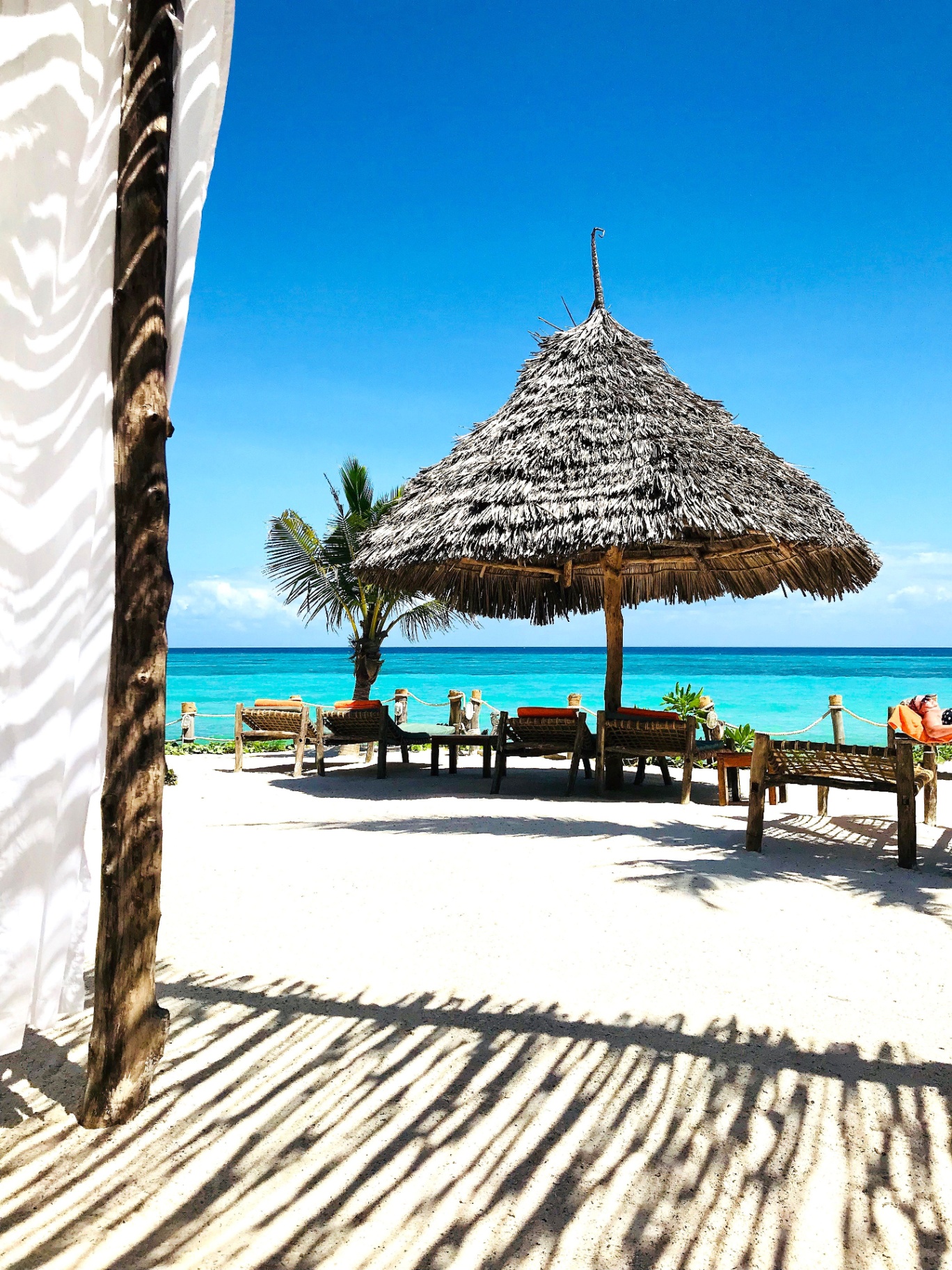 Palapa de paja y tumbonas sobre arena blanca frente al mar turquesa de Zanzíbar, Tanzania